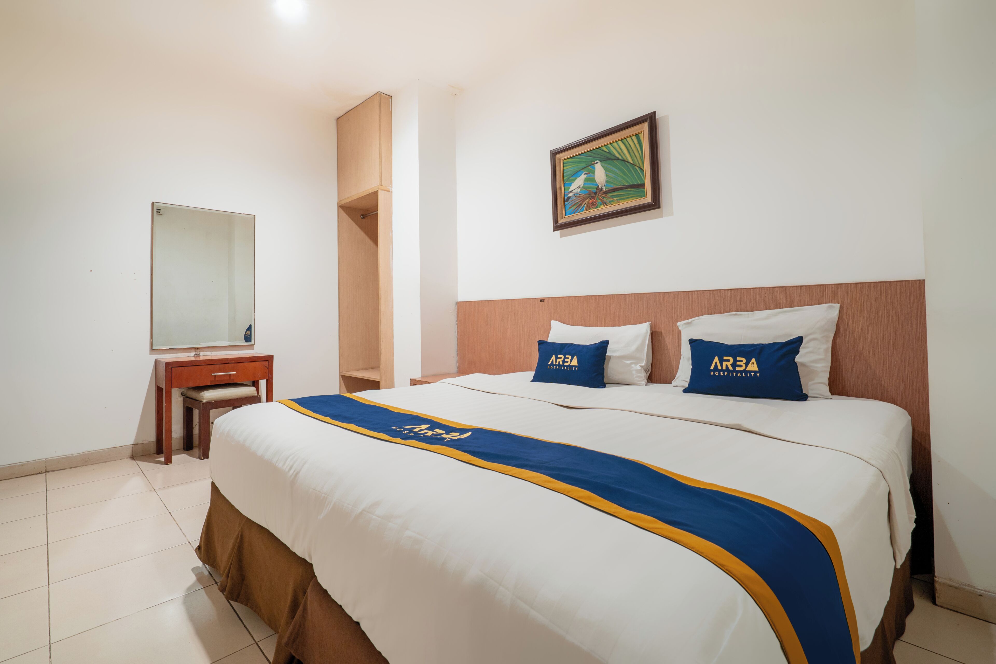 A hotel room with a bed, a desk, a chair, a mirror, and a painting on the wall.