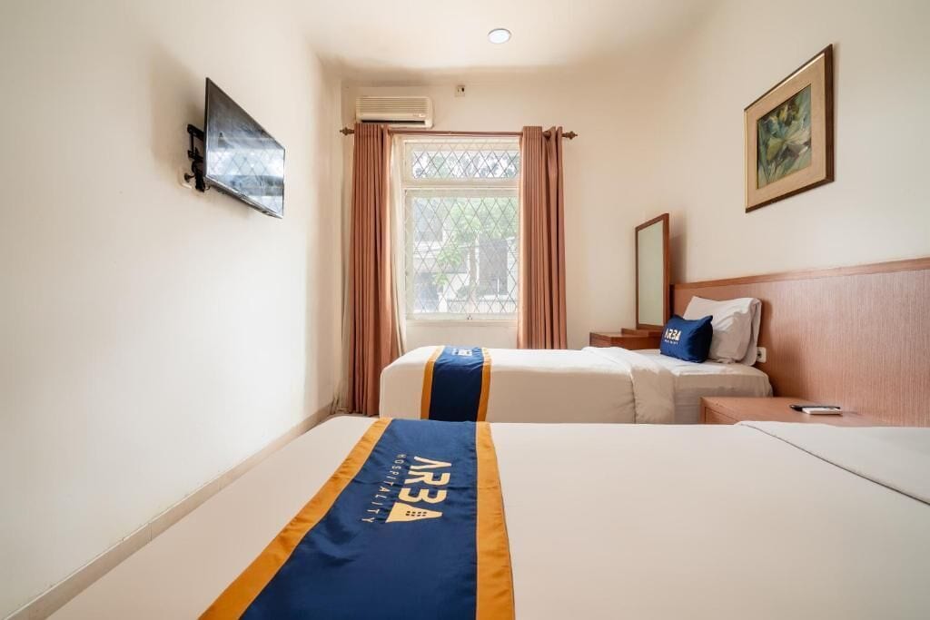 Une chambre d’hôtel avec deux lits, une télévision, une fenêtre avec des rideaux, un tableau au mur et un appareil de climatisation.