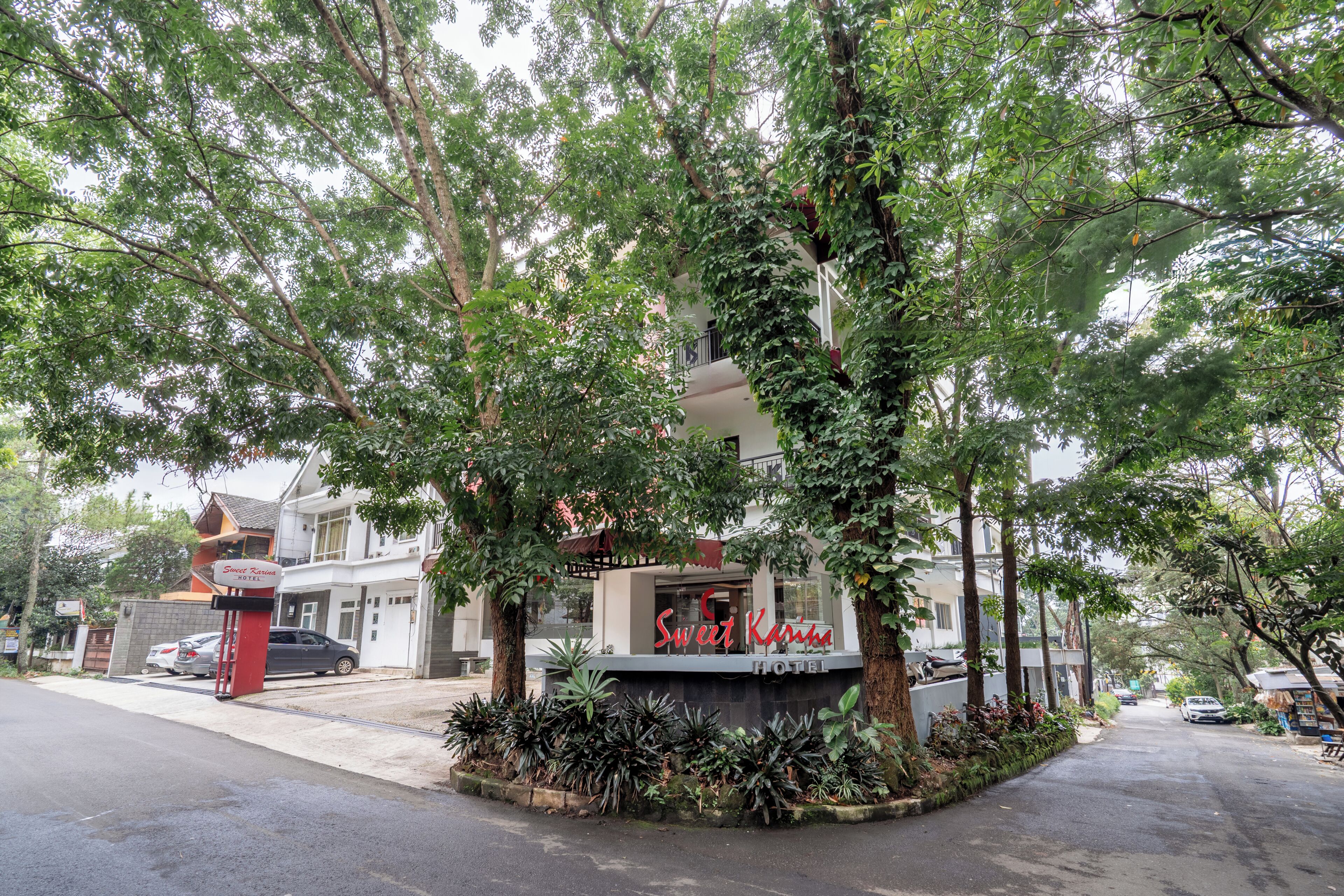A hotel named 'Sweet Karma' with a signboard, surrounded by lush greenery and trees.