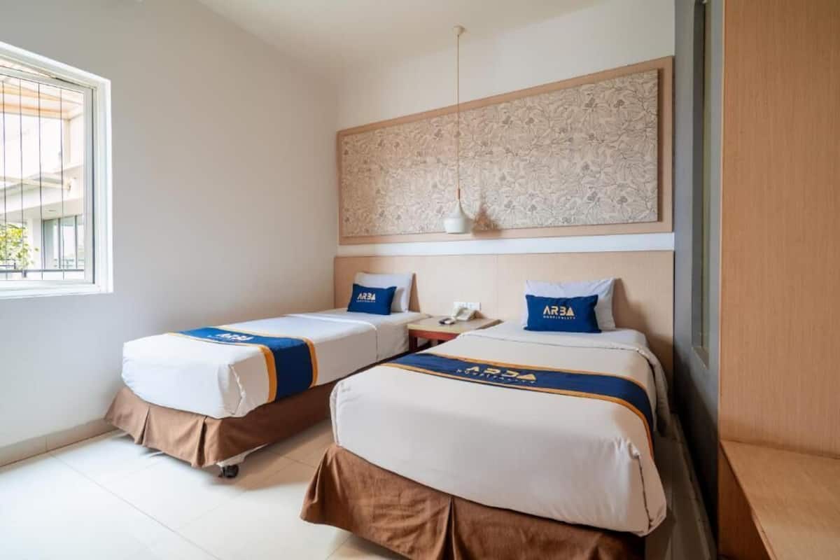 Ein Hotelzimmer mit zwei Betten, einem Fenster, einem Wandbild und einer Pendelleuchte.