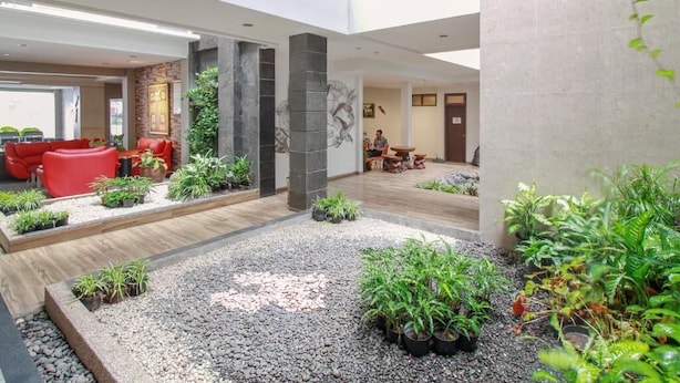 A spacious indoor area with a seating area, plants, and a stone pillar. - Sweet Karina Hotel Pasteur (Bandung)