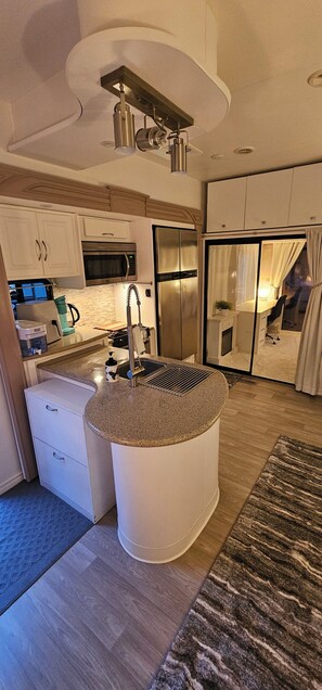Een moderne keuken met een centraal eiland, roestvrijstalen apparatuur en uitzicht op een slaapkamer.