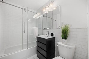 A modern bathroom with a glass shower enclosure, a black vanity, a white toilet, and a potted plant. - The Lenox - 3rd Floor (New York)