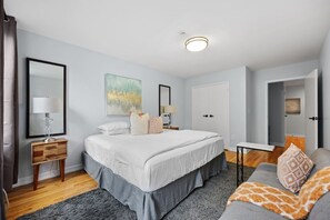 A bedroom with a bed, bedside tables, a nightstand, a dresser, a mirror, a painting, and a door. - The Lenox - 3rd Floor (New York)