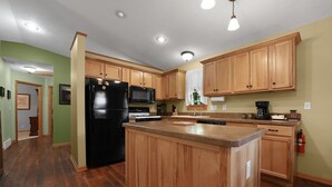 A kitchen with wooden cabinets, a black refrigerator, a microwave, and a coffee maker. - Traverse City M-22 Cottage | Hot Tub, Beach Access (Traverse City)