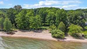A beach with a forested hill in the background. - Traverse City M-22 Cottage | Hot Tub, Beach Access (Traverse City)