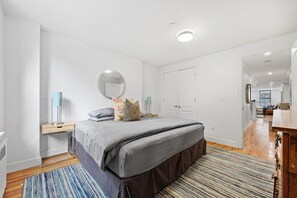 Ein Schlafzimmer mit Bett, Nachttischen, einem Spiegel und einer Tür zu einem anderen Raum.