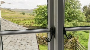 A window view of a rural landscape with stone walls, a stone building, and a tree.