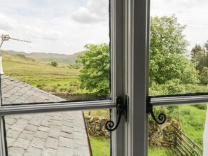 A window view of a rural landscape with stone walls, a stone building, and a tree.