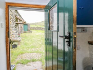 Une porte qui mène à un bâtiment en pierre, avec un chemin de pierre et une cour gazonnée.