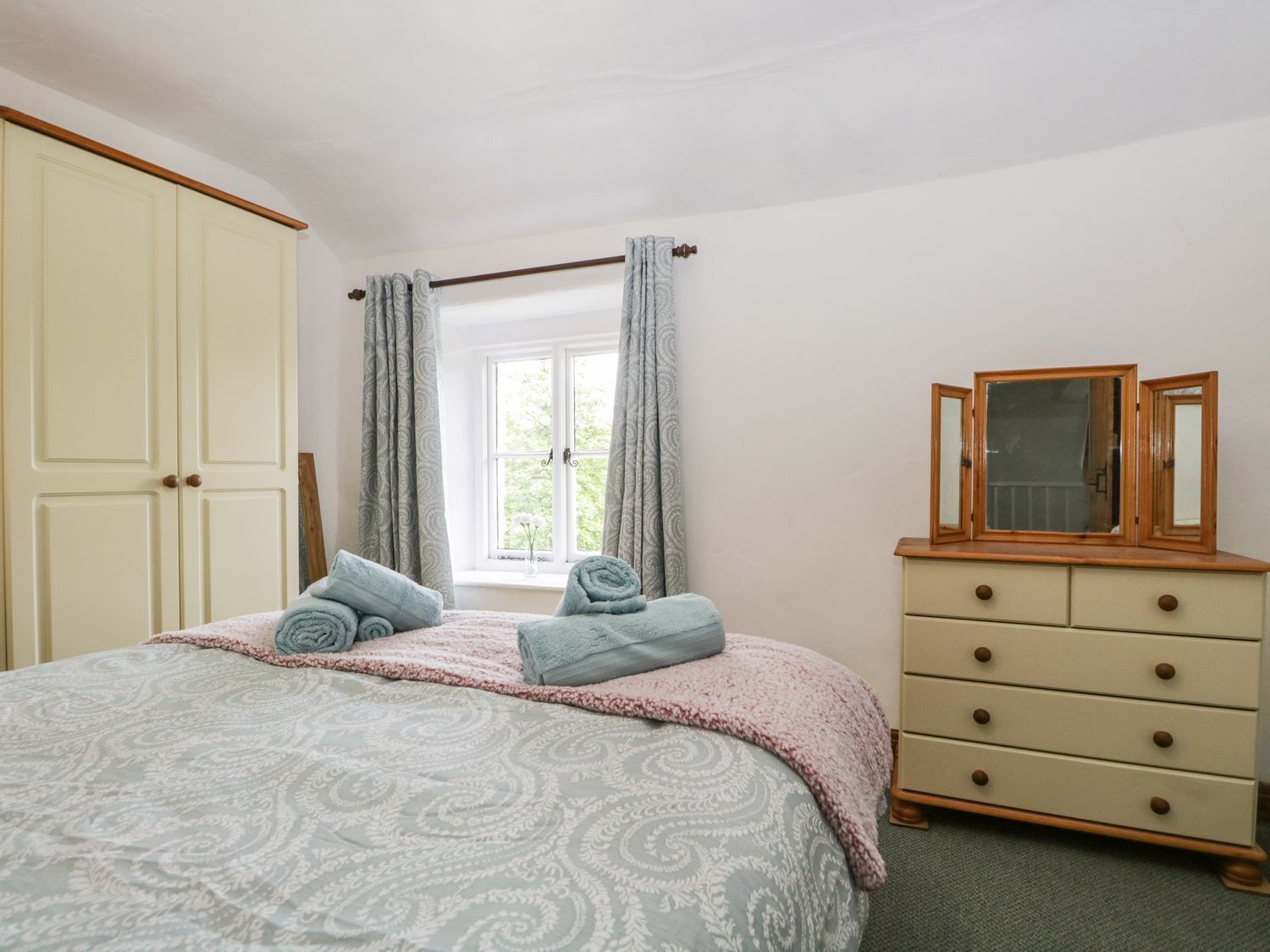 Un dormitorio con cama, cómoda, ventana con cortinas y espejo.