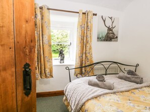A bedroom with a bed, a window with curtains, a wall-mounted picture of a deer, and a wooden door.