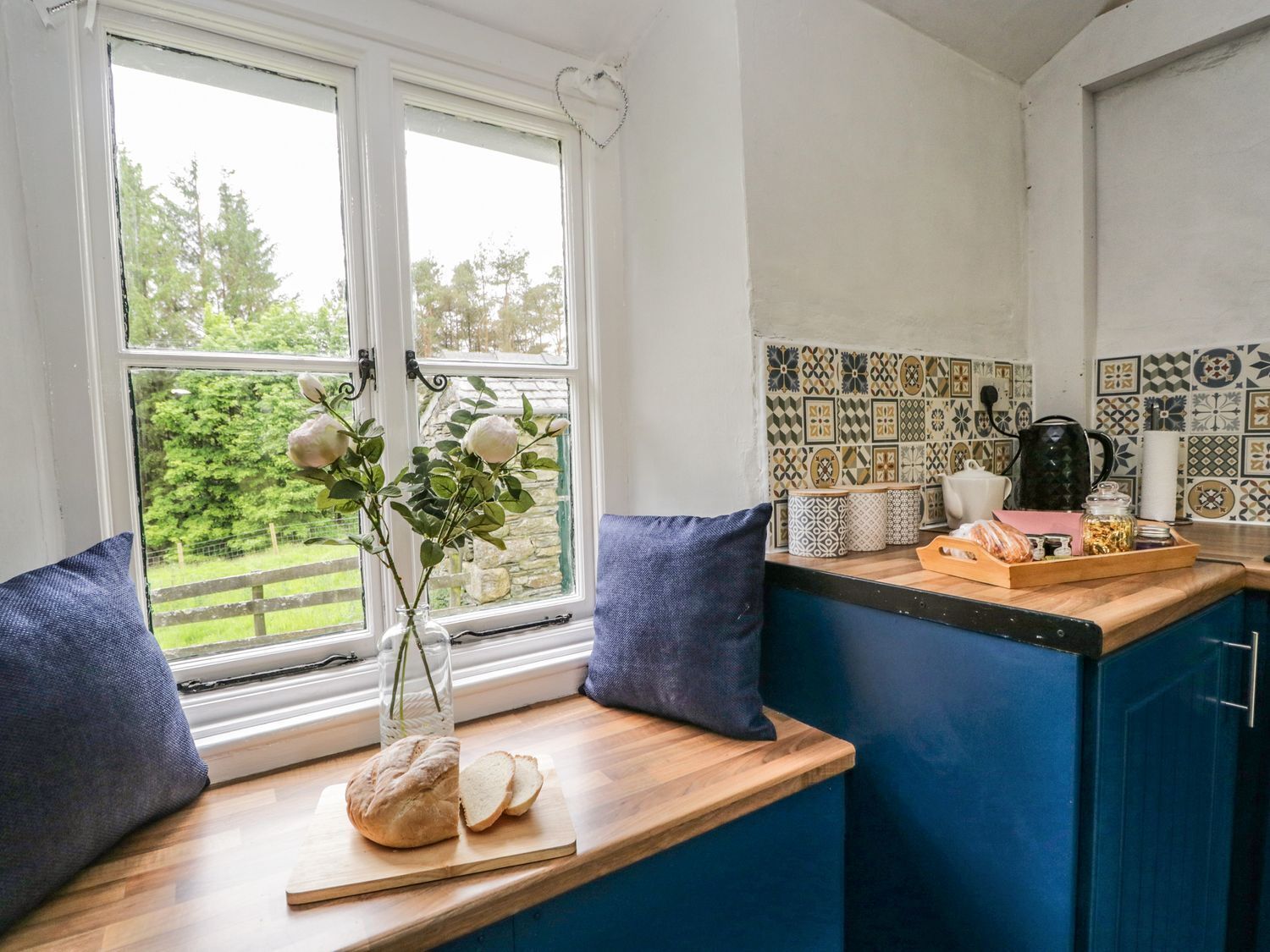 A kitchen with a wooden countertop, a vase with flowers, and a window with a view of greenery.