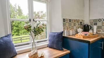 A kitchen with a wooden countertop, a vase with flowers, and a window with a view of greenery.