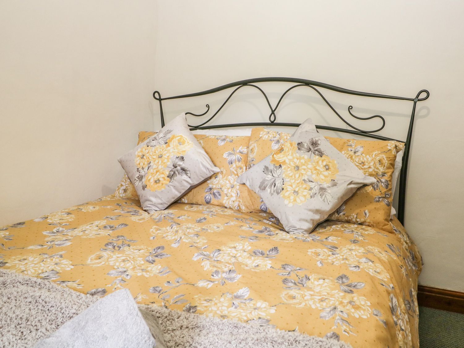 A bed with a floral bedspread and two pillows, a metal headboard, and a white wall.