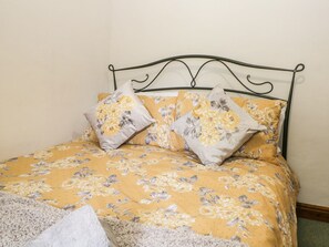Een bed met een bloemenprint sprei en twee kussens, een metalen hoofdbord en een witte muur.
