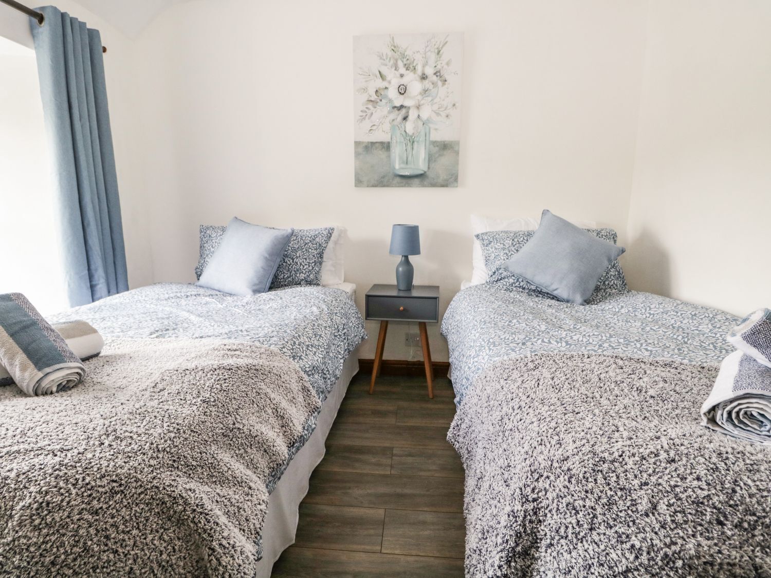 A bedroom with two beds, a nightstand, a lamp, and a painting on the wall.
