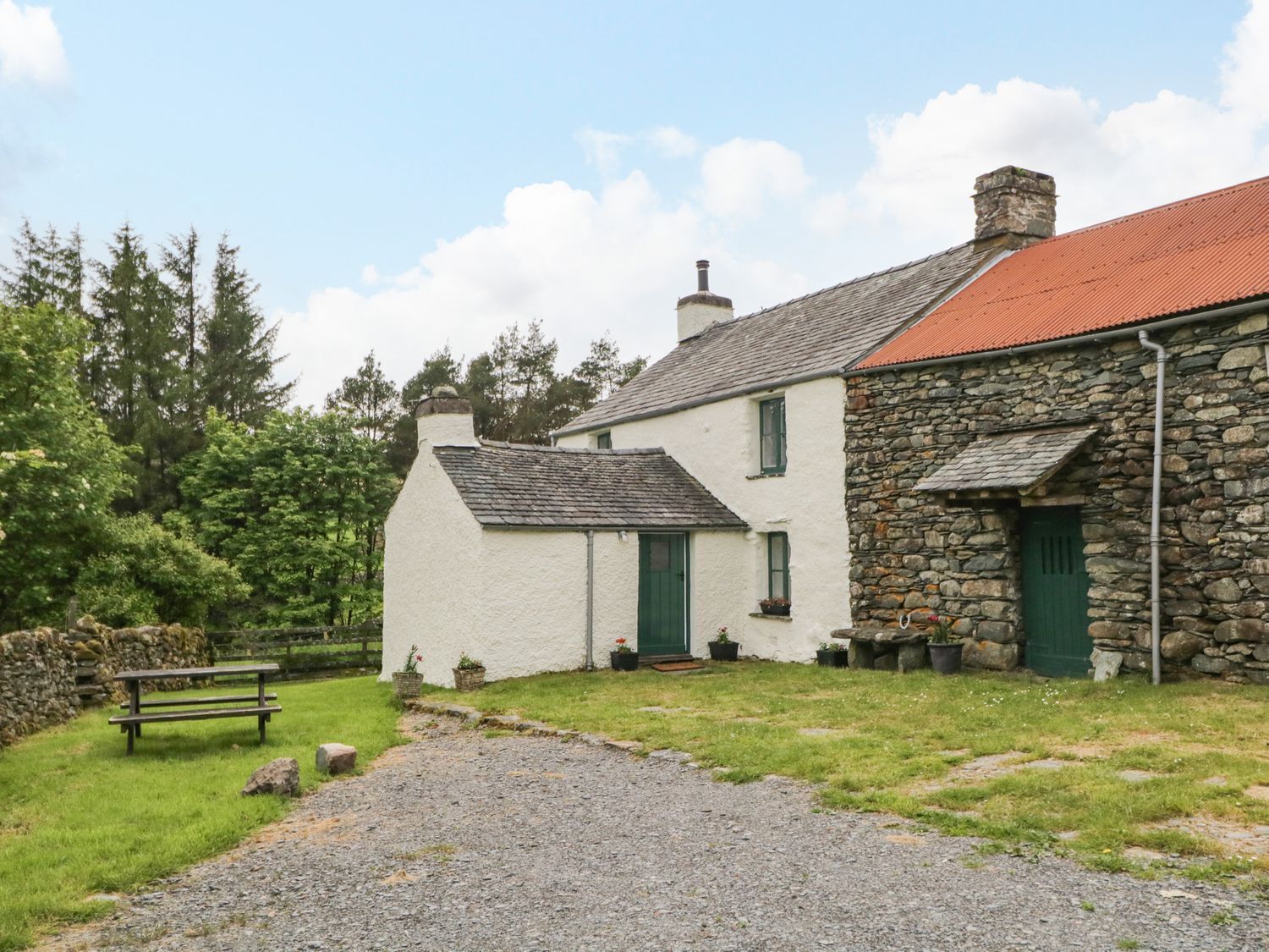 A stone house with a white exterior and green doors, a gravel path, and a bench.