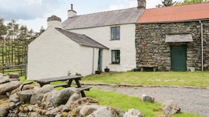 A white house with a stone extension, a stone wall, and a wooden bench.
