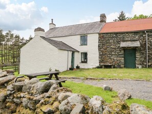 A white house with a stone extension, a stone wall, and a wooden bench.
