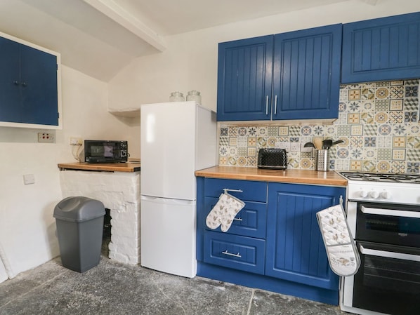 A kitchen with blue cabinets, a white refrigerator, a microwave, a stove, and a trash bin.