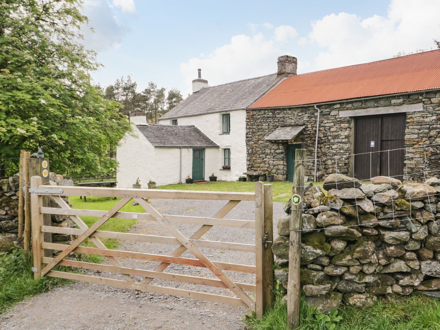 A rural property with a stone wall, a wooden gate, and a white house with a red roof.