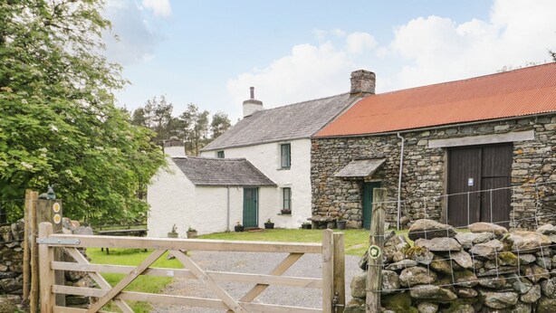 A rural property with a stone wall, a wooden gate, and a white house with a red roof.
