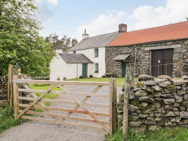 A rural property with a stone wall, a wooden gate, and a white house with a red roof.