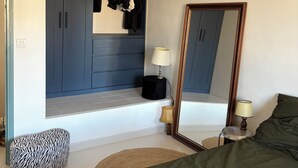 Un dormitorio con cama, armario, espejo y una mesita de noche con lámparas.