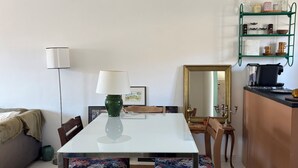 Un comedor con una mesa blanca, dos sillas, un jarrón verde y un espejo en la pared.