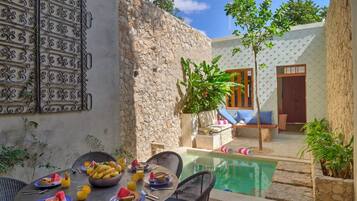 Un espace repas avec une piscine, des murs en pierre et des sièges d’extérieur.
