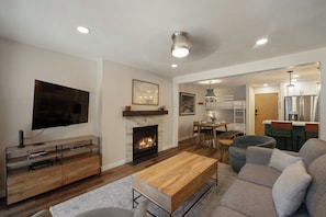 Ein modernes Wohnzimmer mit Kamin, Flachbildfernseher, Couchtisch aus Holz und einer Couch.