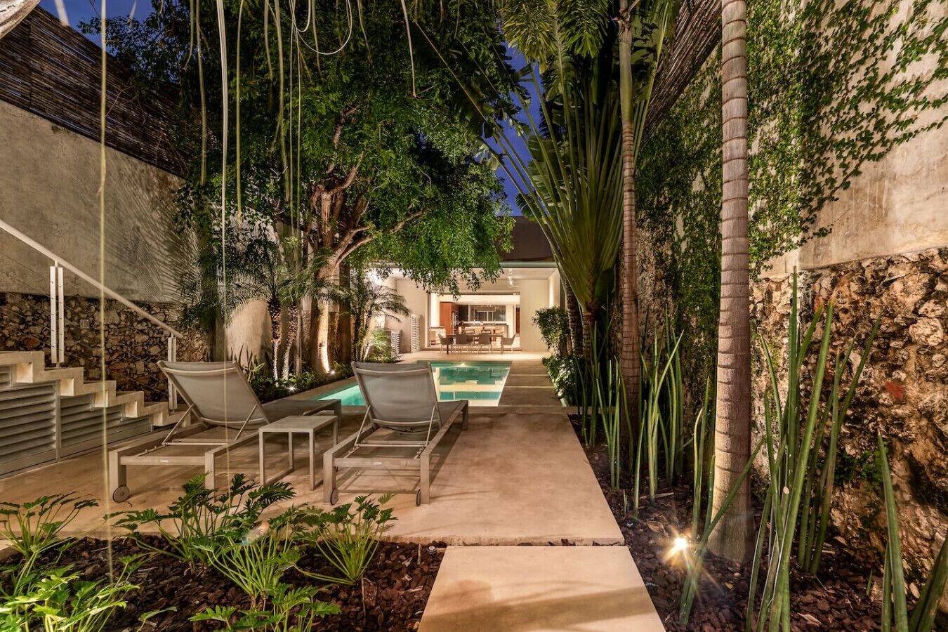 A pool area with lounge chairs, a staircase, and a view of a house.