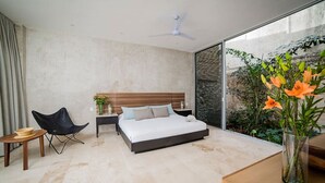 Un dormitorio moderno con cama, una silla, una mesita de noche y un ventanal con vistas a la vegetación.