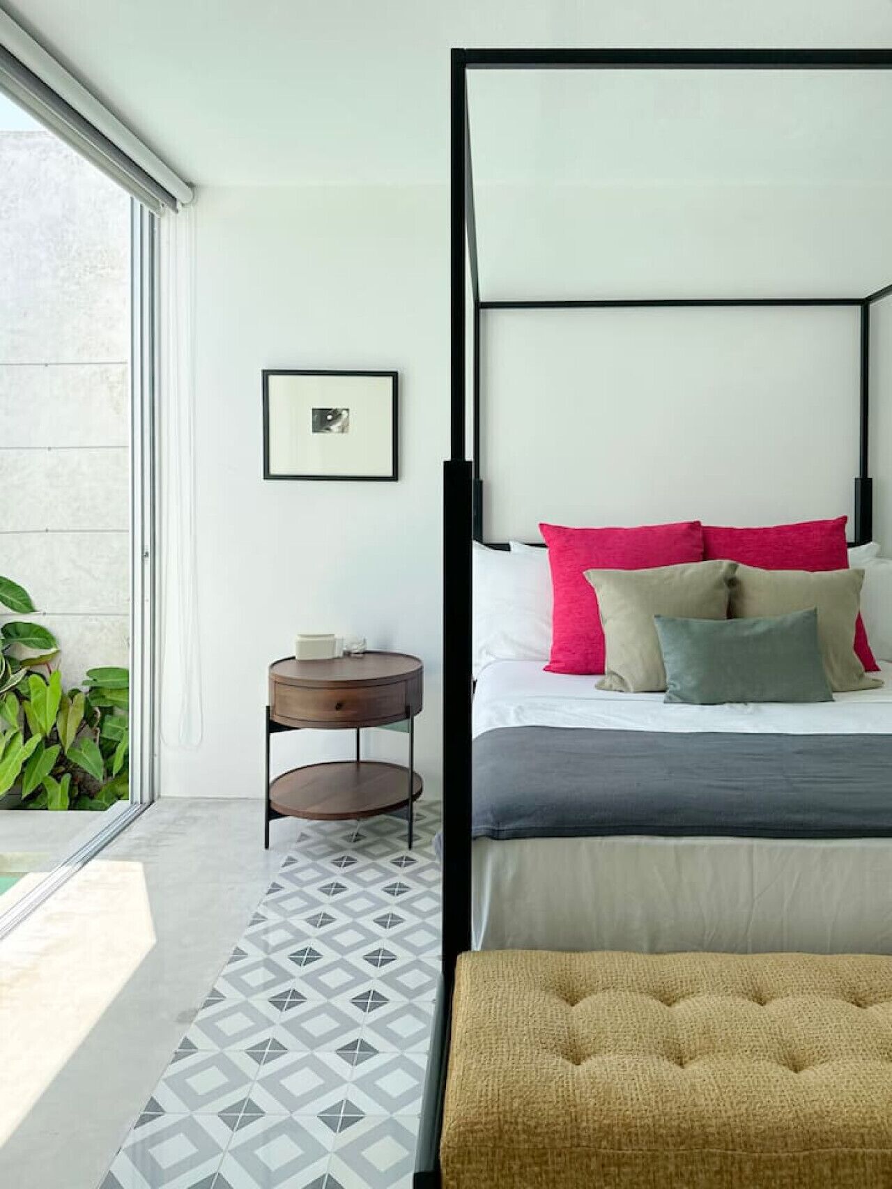Un dormitorio moderno con una cama con dosel, una mesita redonda pequeña, un cuadro enmarcado en la pared y una alfombra con diseño geométrico.