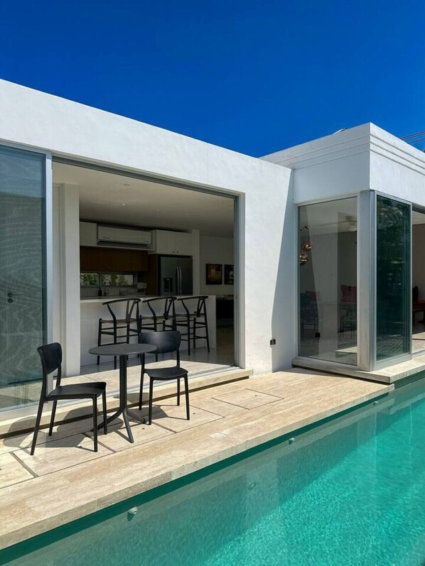 Ein modernes Haus mit Pool, offener Küche und Essbereich mit Gartenmöbeln.