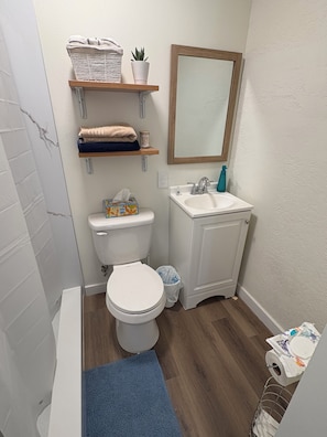 Een badkamer met toilet, wastafel, spiegel en planken met handdoeken en een potplant.