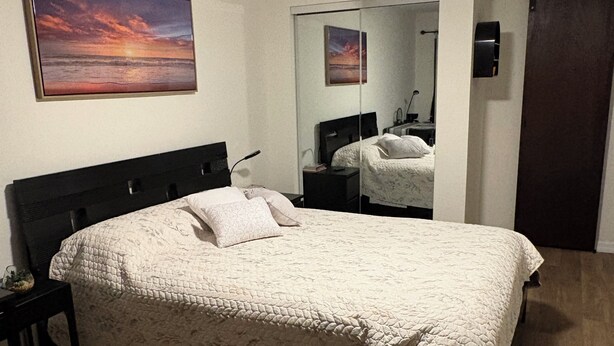 Een slaapkamer met een bed, nachtkastje, bureau, plafondventilator en een schilderij aan de muur.