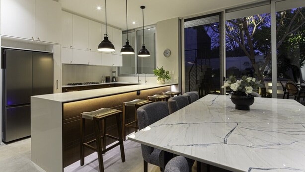 Een moderne keuken met een centraal eiland, barkrukken en een grote eettafel.