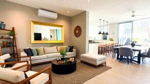 Een moderne woonkamer met een bank, salontafel en stoelen, een eethoek met een tafel en stoelen, en een keuken op de achtergrond.
