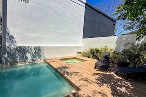 A modern outdoor pool area with a wooden deck, two lounge chairs, and a small hot tub. - Casa Naranjas · Design Home · Pool & Jacuzzi (Merida)