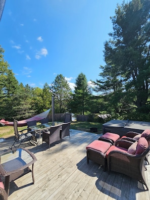 A wooden deck with wicker furniture, a hammock, and a glass table.