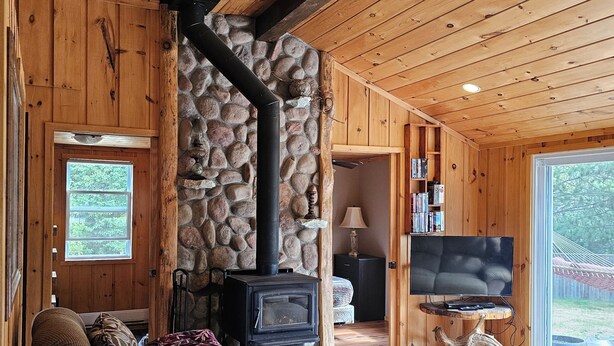 A cozy cabin interior with a stone fireplace, wooden walls, a dining table, and a television. - FALLS VIEW HAVEN (Gilmour)