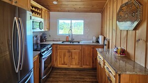 A kitchen with wooden cabinets, a stainless steel refrigerator, a microwave, and a sink. - FALLS VIEW HAVEN (Gilmour)