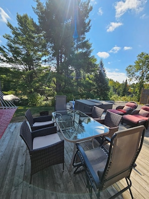 Une terrasse extérieure dotée d’une table à plateau de verre et de chaises en osier, le tout entouré d’arbres.