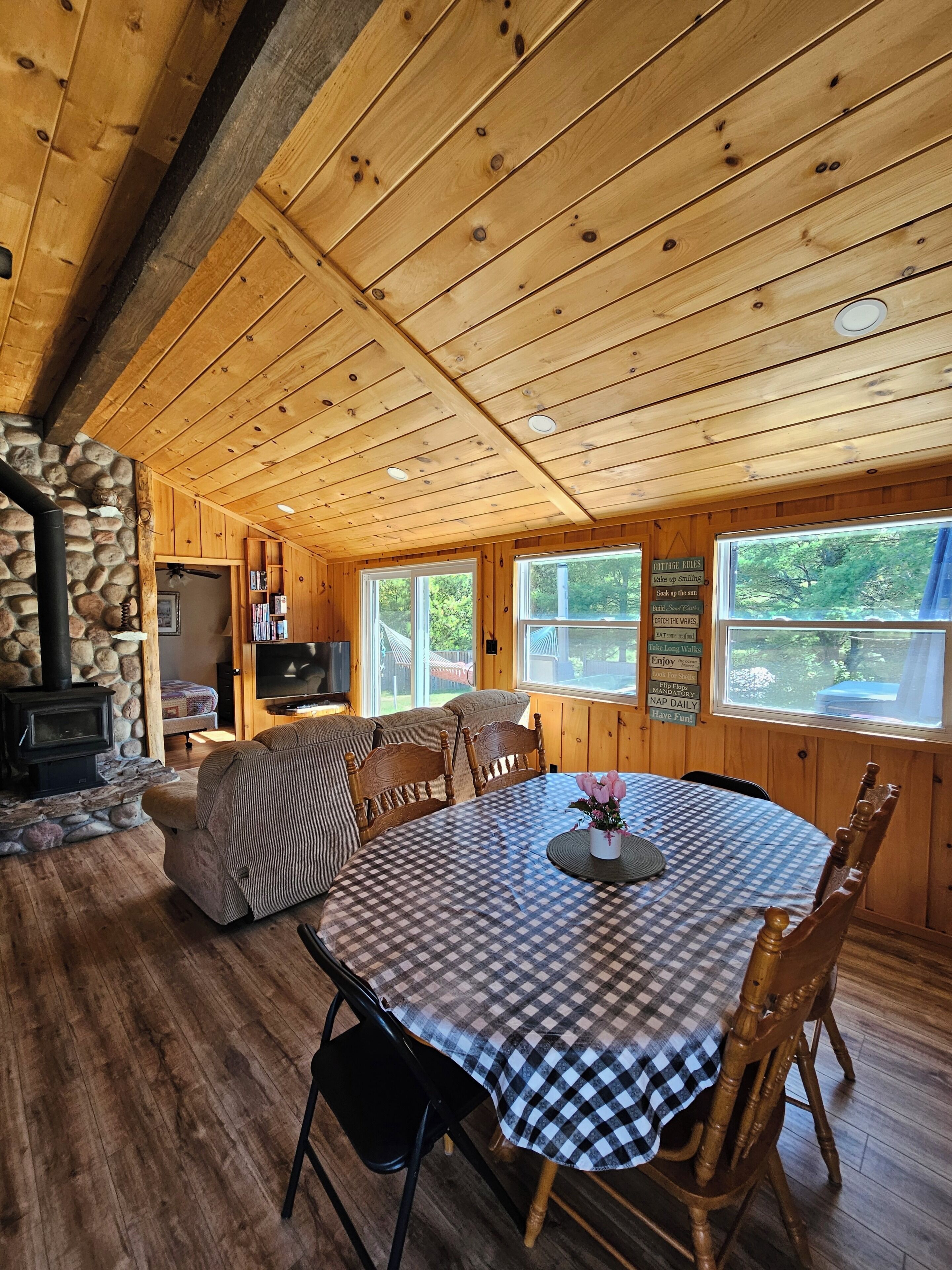 Interior d'una cabana acollidora amb una llar de pedra, sostre de fusta i taula rodona per dinar amb mantell a quadres.