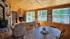 A cozy cabin interior with a stone fireplace, wooden ceiling, and a round dining table with checkered tablecloth. - FALLS VIEW HAVEN (Gilmour)