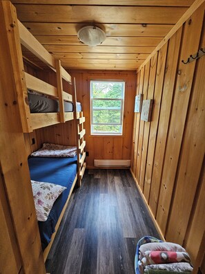 A compact wooden cabin room with bunk beds, a window, and a heater. - FALLS VIEW HAVEN (Gilmour)