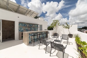 Eine Dachterrasse mit Barbereich, Sitzgelegenheiten und Kübelpflanzen.