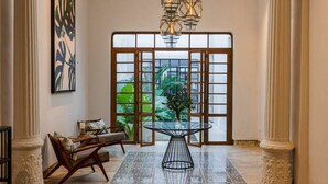 Een ruime lobby met een glazen tafel, een hanglamp en een groot raam met uitzicht op groen.